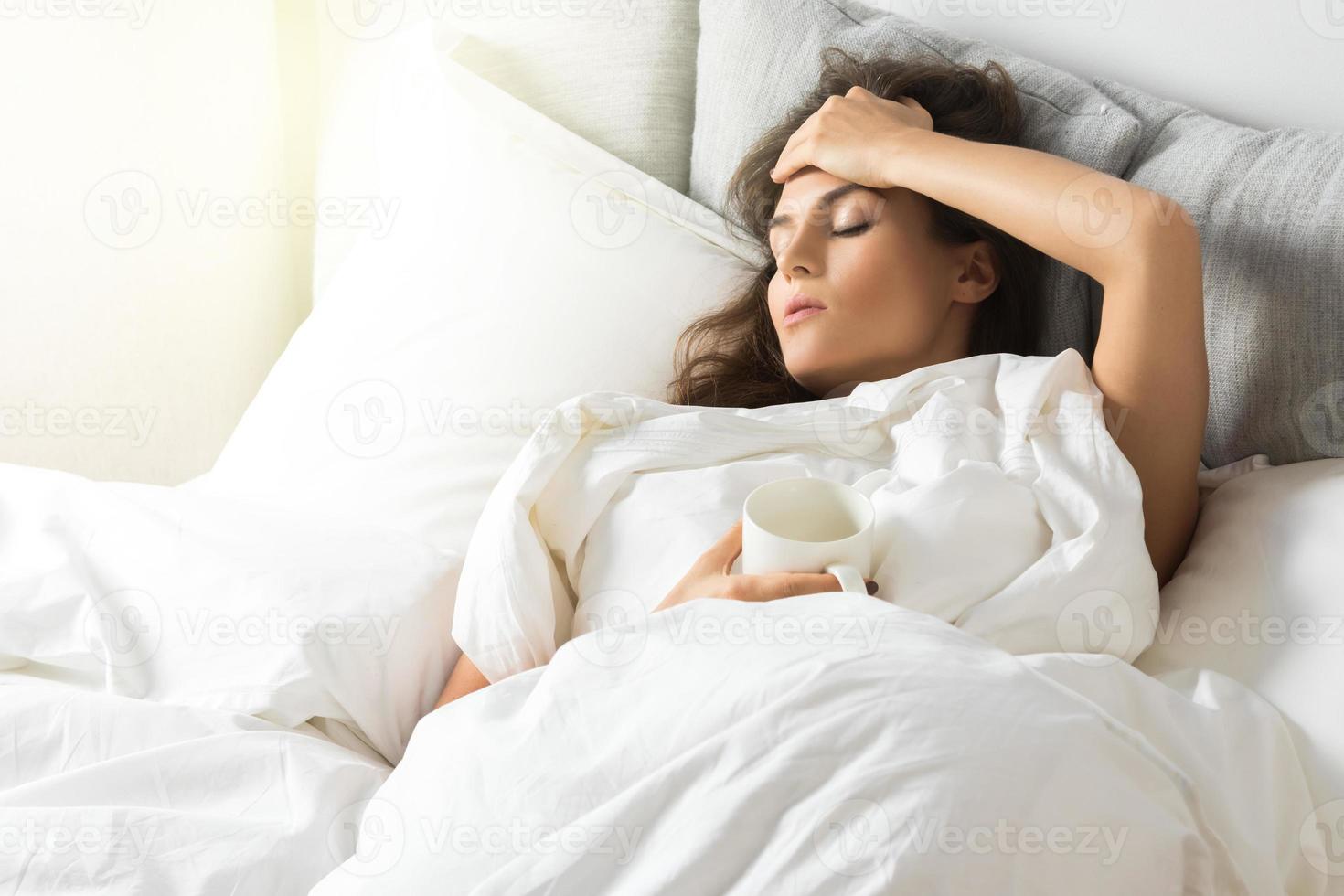 femme malade sous couverture avec une tasse de boisson chaude photo