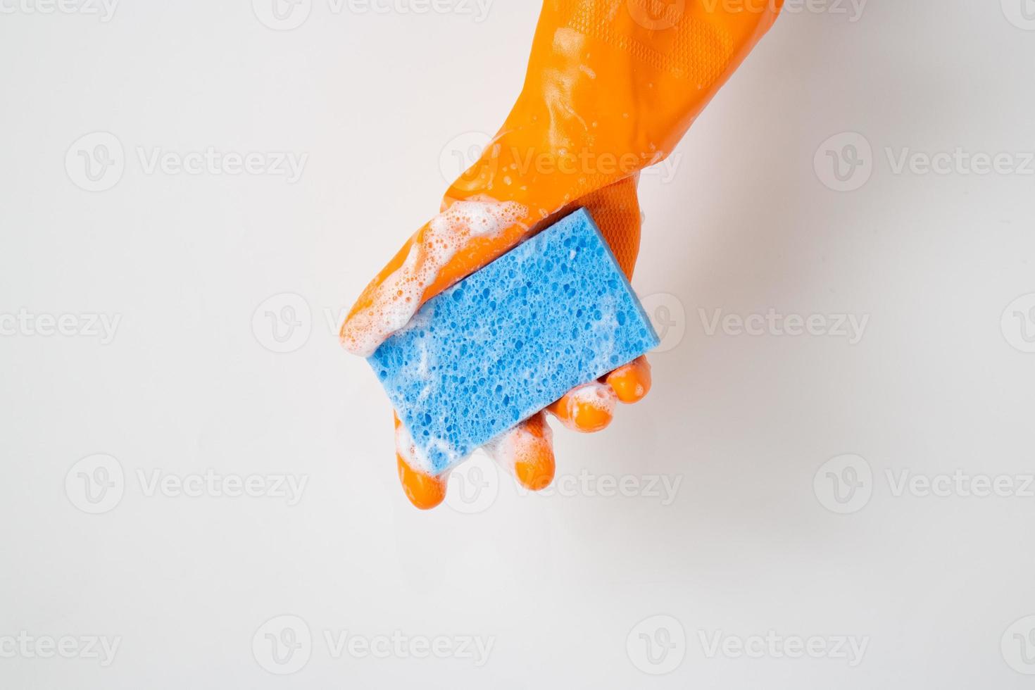 concept de nettoyage, main dans des gants en caoutchouc orange et tenant une éponge bleu clair avec de la mousse pour le nettoyage photo