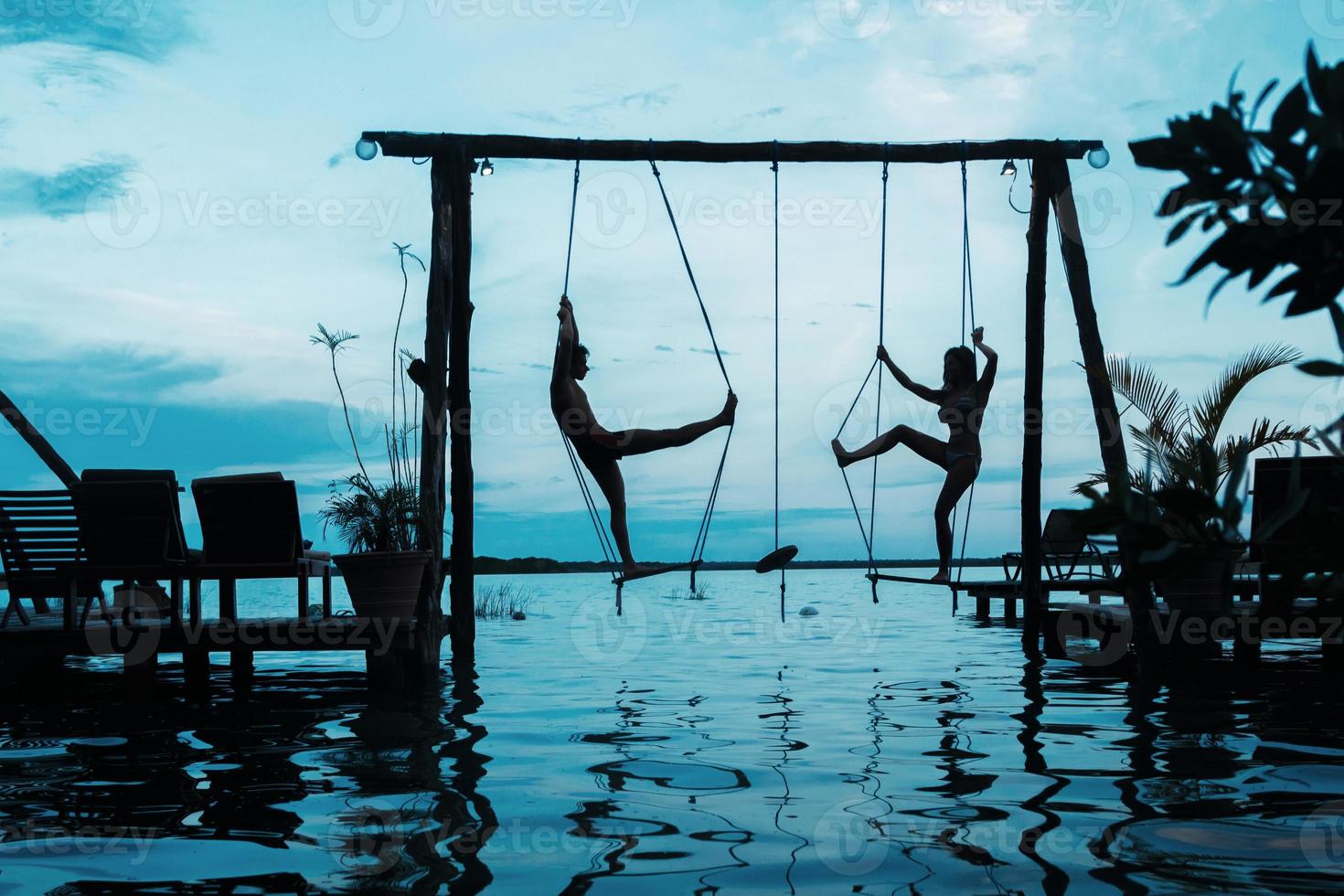 silhouette de couple sur des balançoires qui est au-dessus de l'eau photo