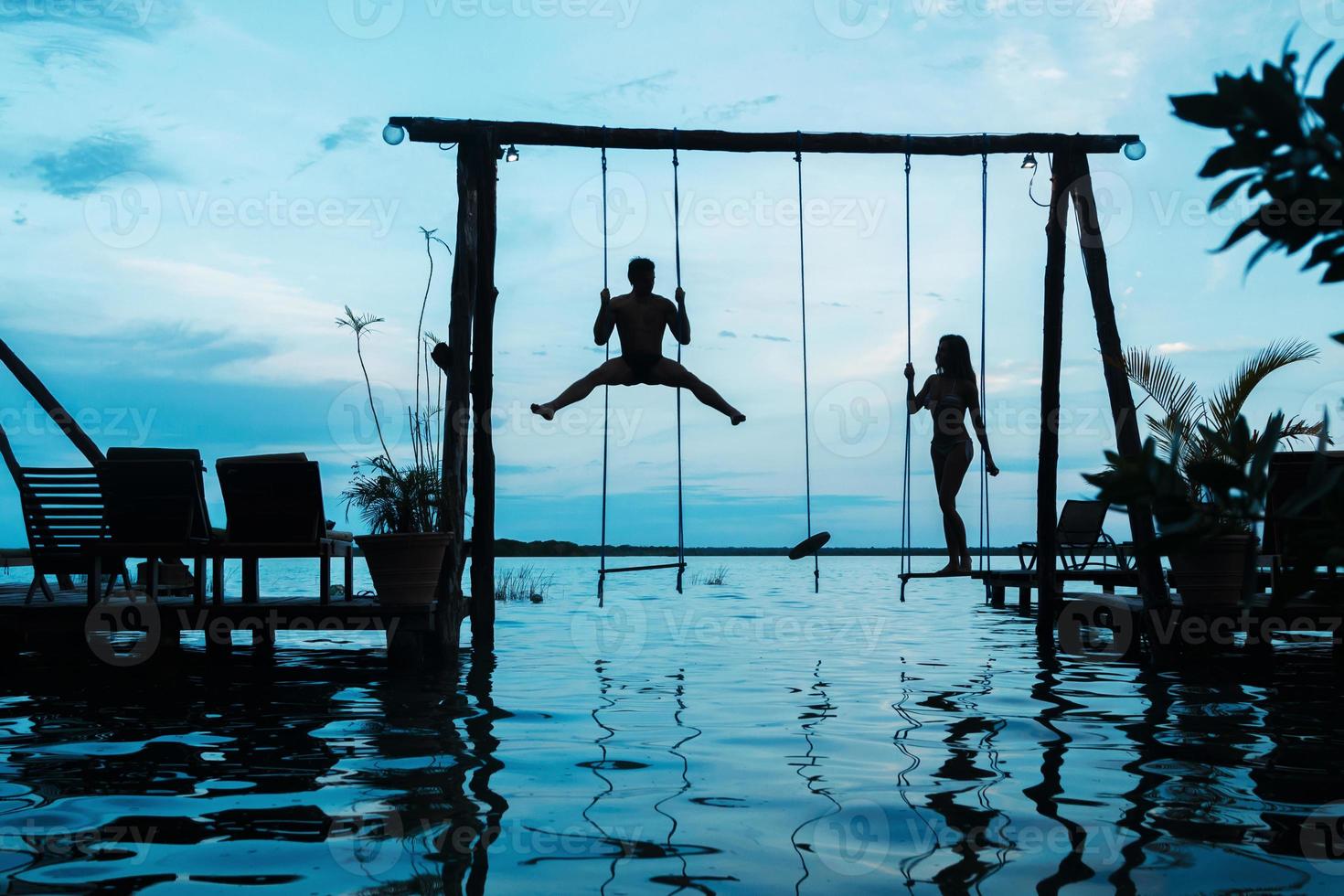 silhouette de couple sur des balançoires qui est au-dessus de l'eau photo