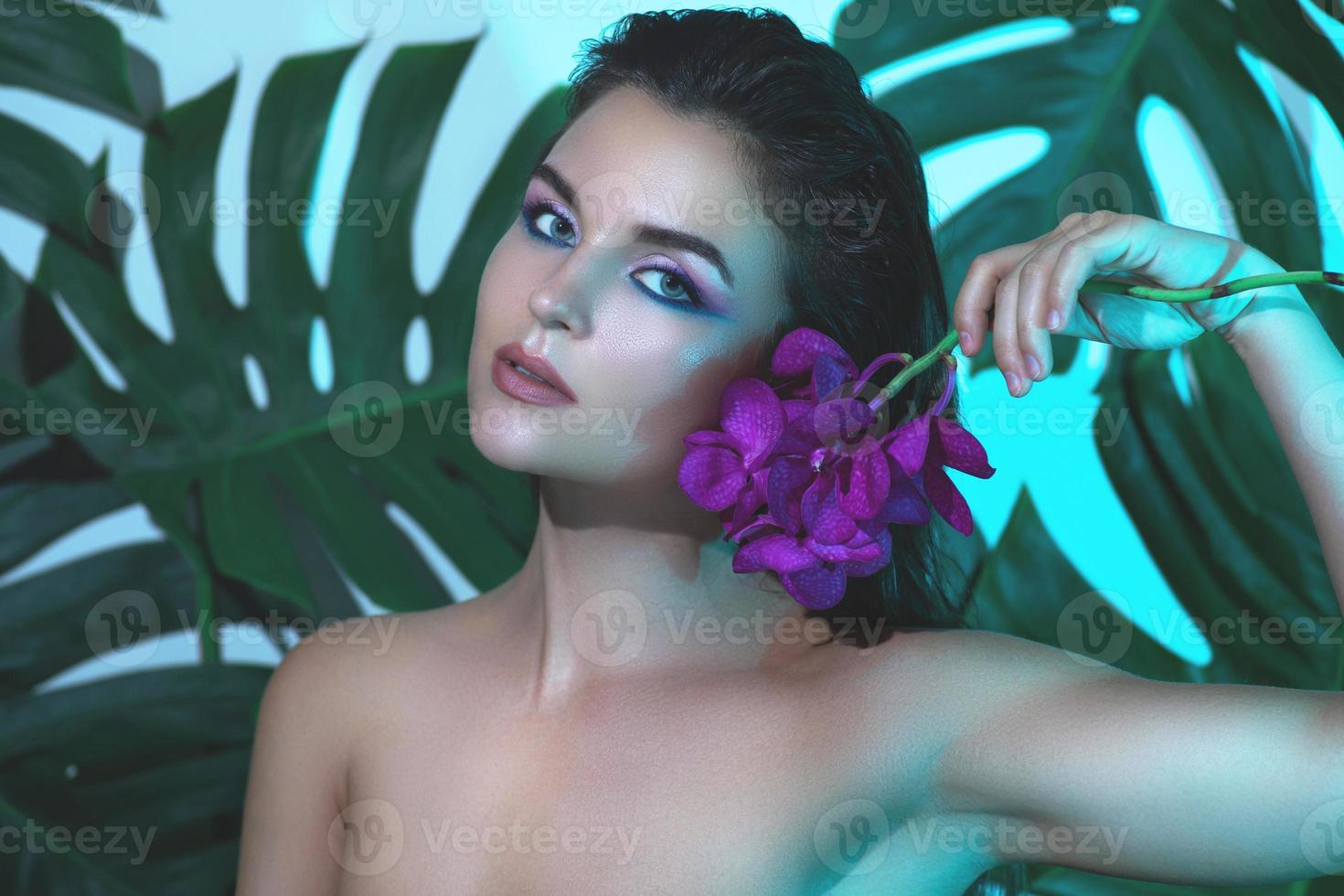 jeune et belle femme avec une peau lisse parfaite tient des fleurs d'orchidées photo