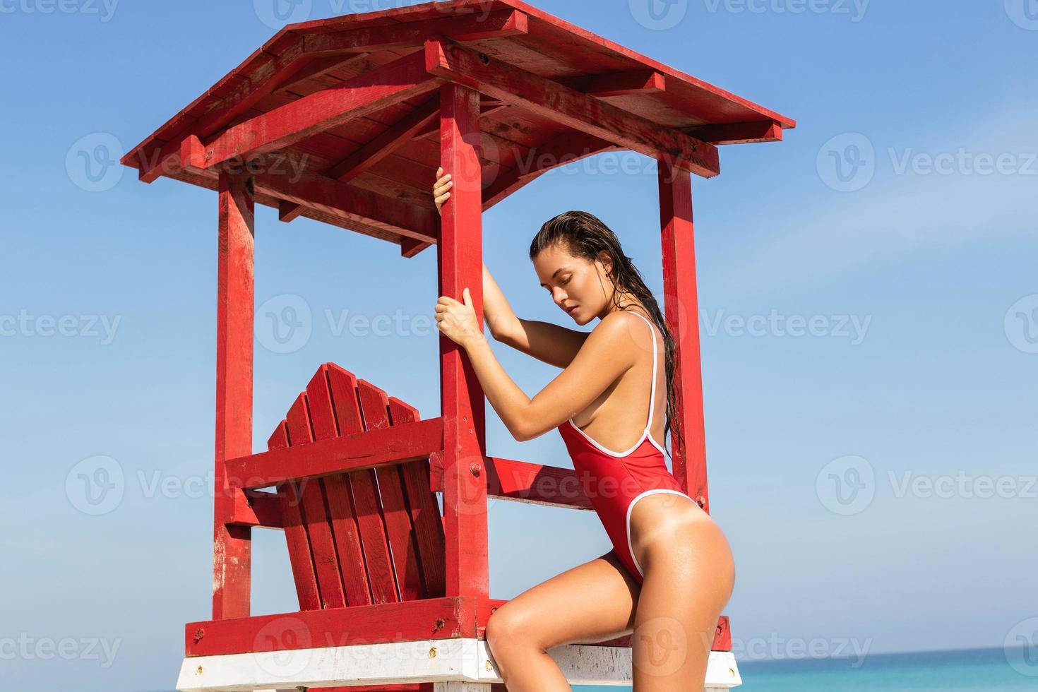 femme sexy en maillot de bain rouge posant à côté d'une tour de sauveteur photo