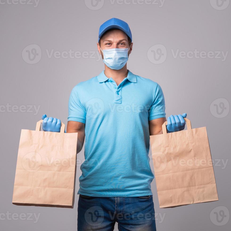 le jeune livreur porte un masque de prévention et des gants avec des sacs en papier photo