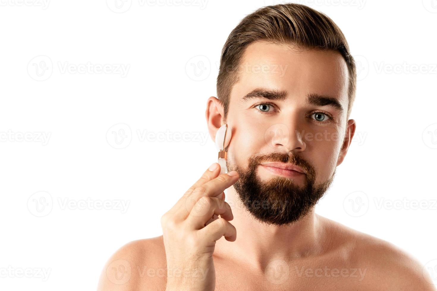 jeune bel homme utilise un rouleau facial pour un massage facial photo