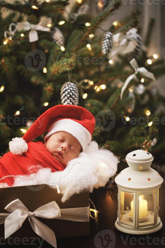 mignon bébé nouveau-né portant un chapeau de père noël dort dans la boîte de cadeau de noël photo