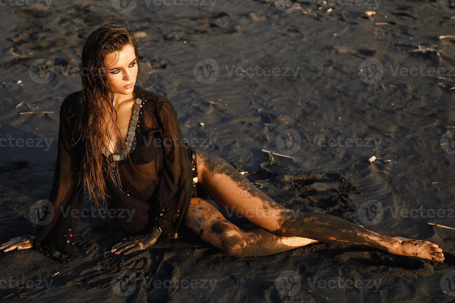 femme sexy portant une tunique noire pose sur la plage avec du sable noir photo