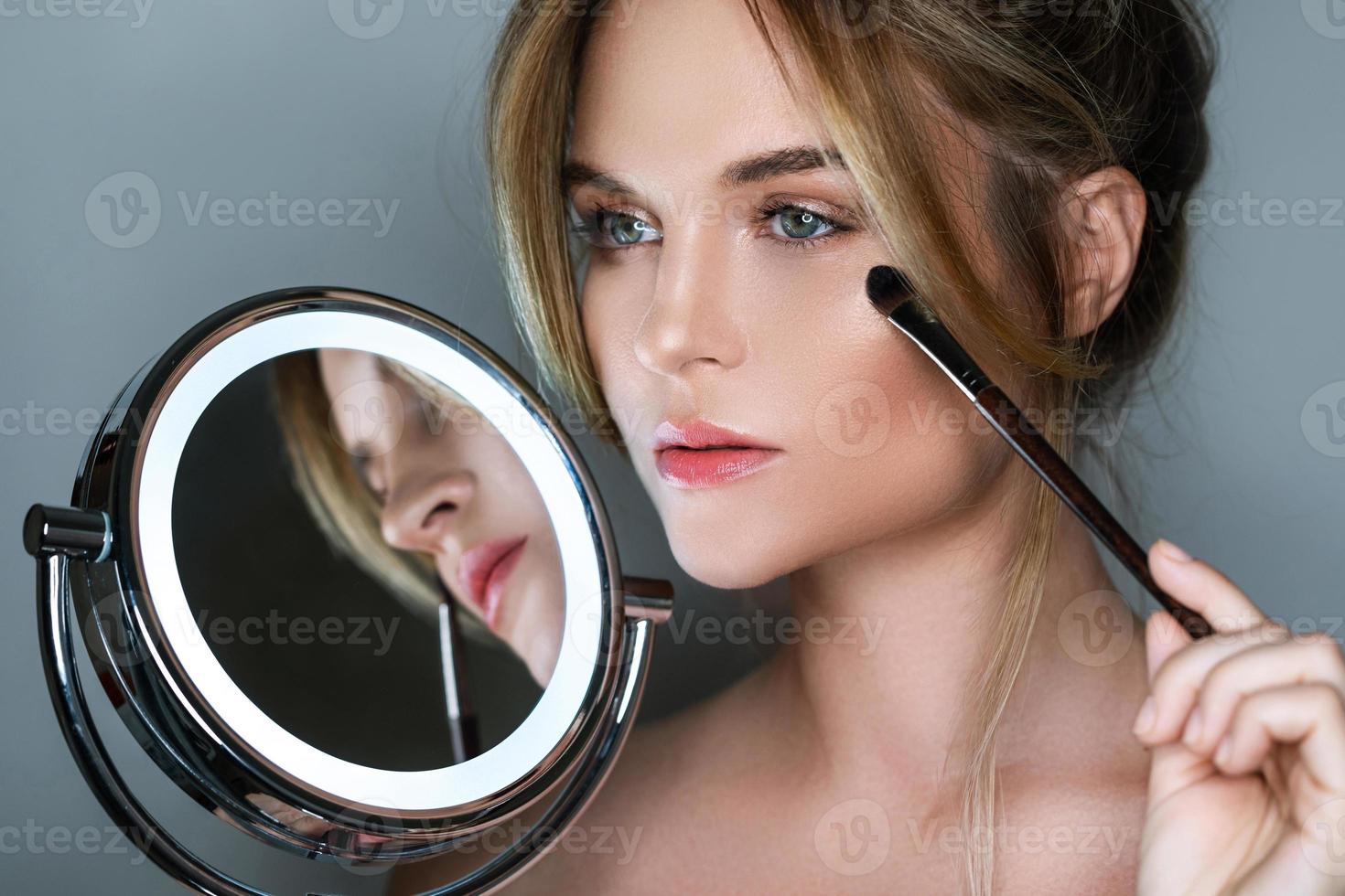 belle femme avec pinceau de maquillage et miroir rond avec lumière led  16251014 Photo de stock chez Vecteezy