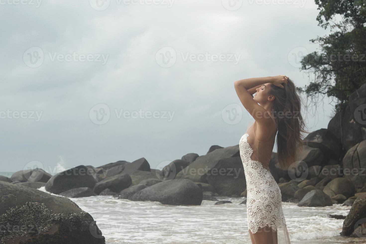 jeune femme vêtue d'une belle robe blanche pose sur la plage photo