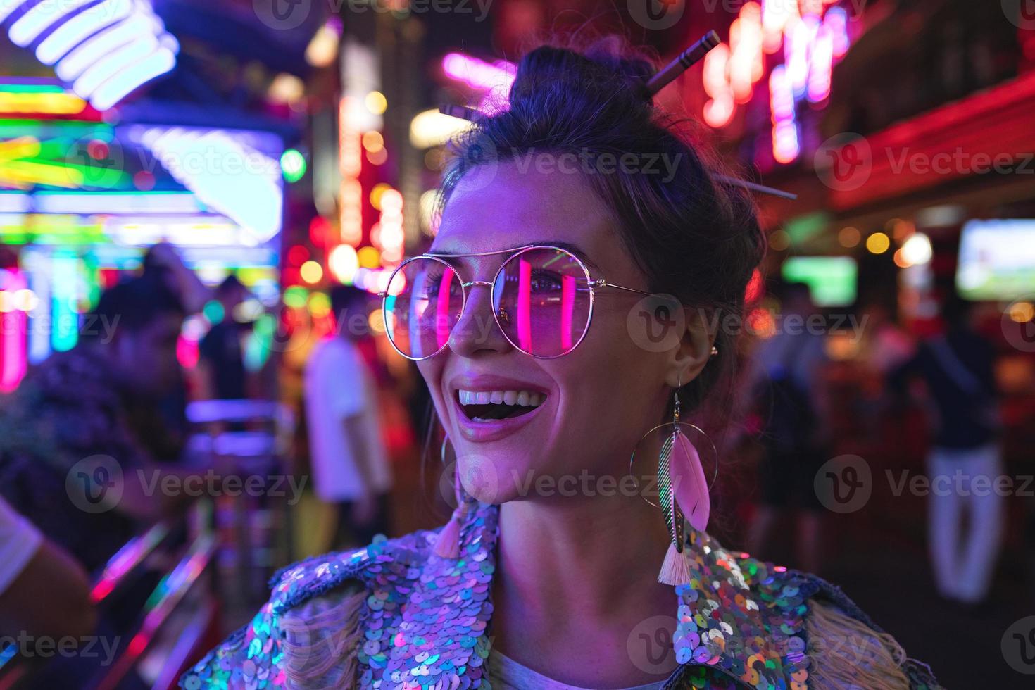 femme élégante portant une veste avec des paillettes brillantes dans la rue de la ville avec des néons photo