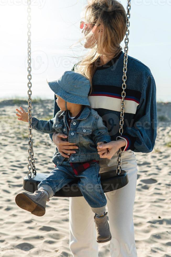 la jeune mère et son fils sur la balançoire regardent la plage. photo