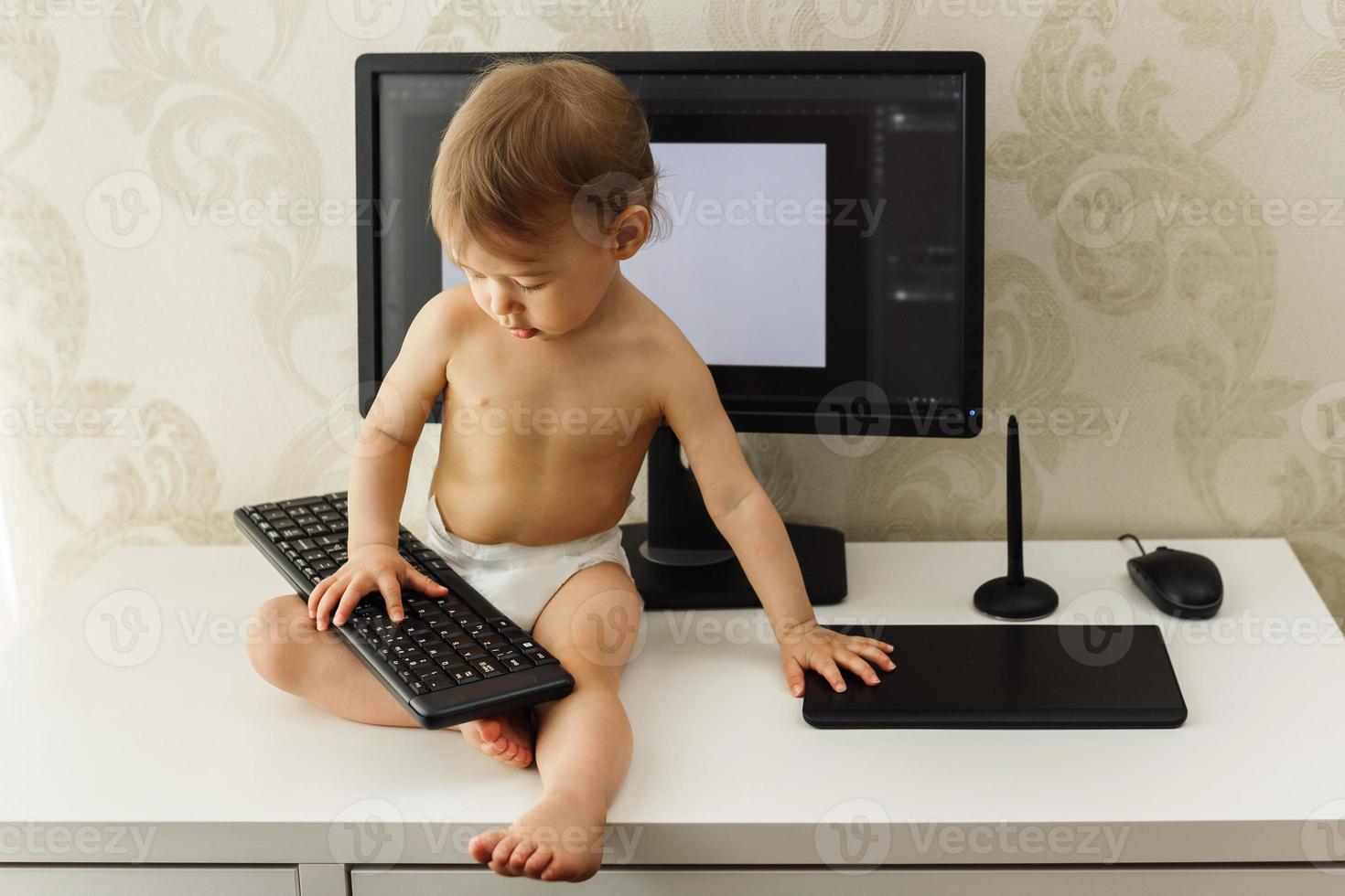 petit garçon assis sur un bureau et jouant avec un clavier. photo