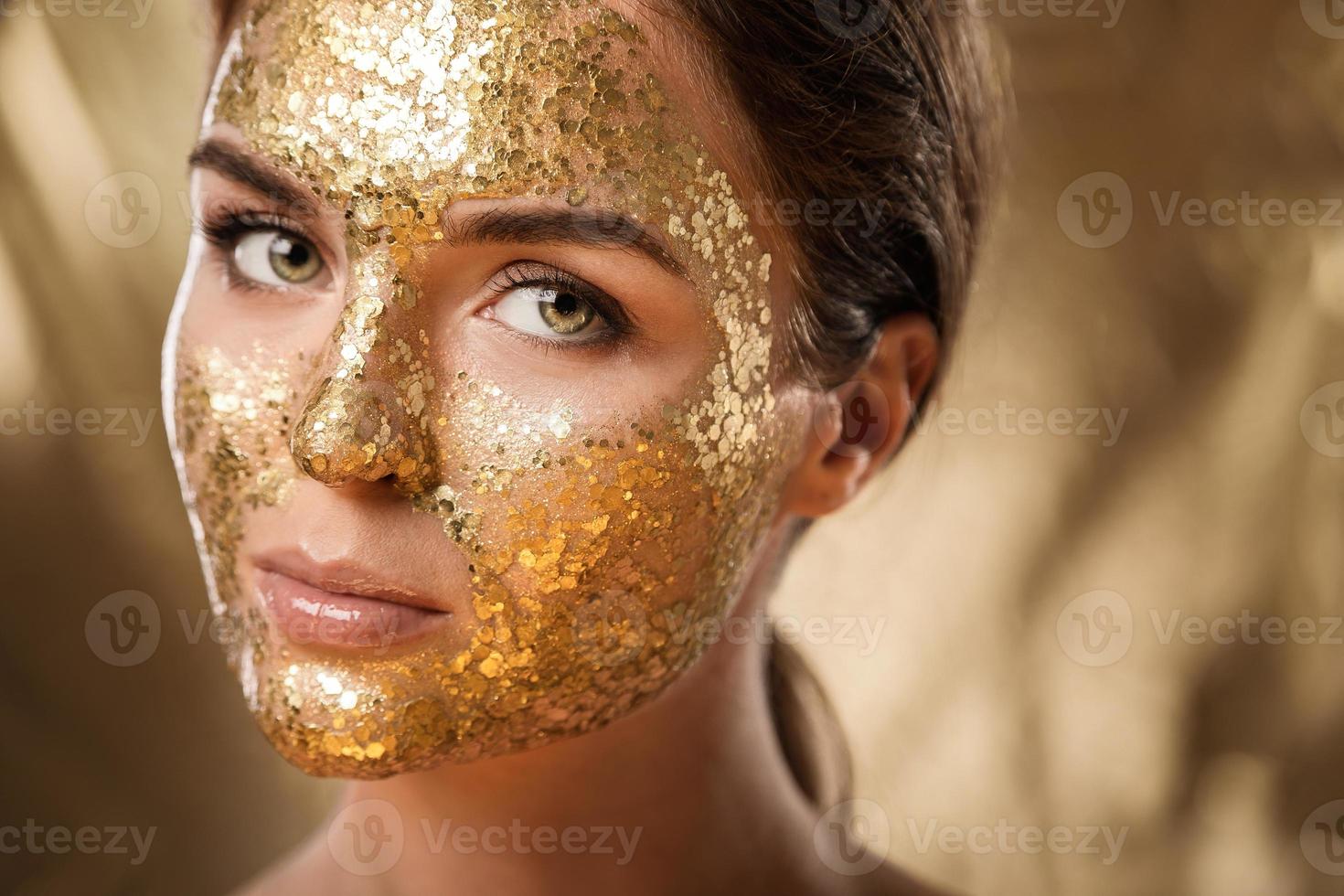 belle femme avec un masque brillant doré sur son visage pour le traitement de la peau photo