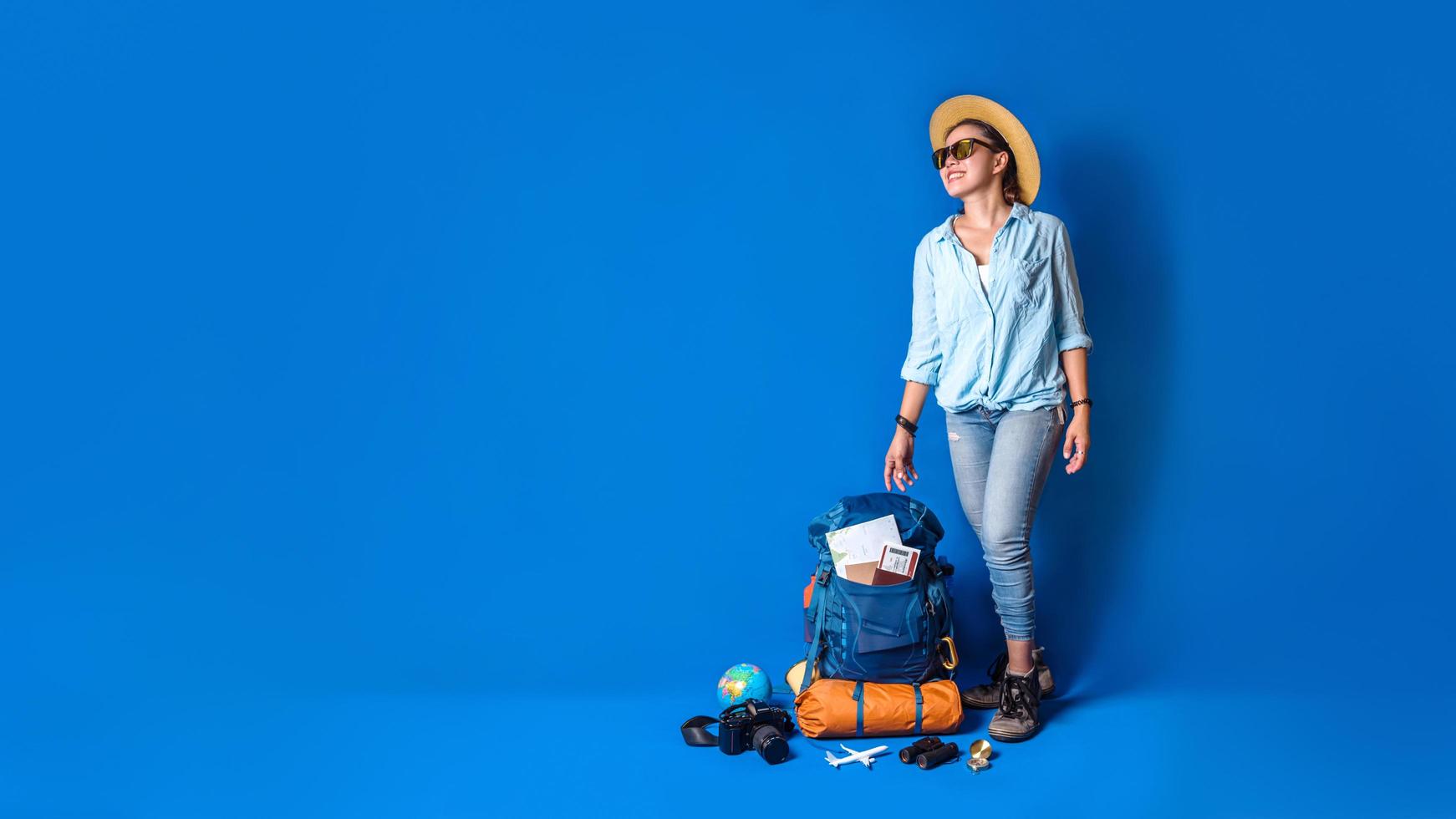 jeune femme heureuse de voyageur asiatique en chemise bleue avec sac à dos avec et équipement pour les vacances des voyageurs avec une carte, sur fond de couleur bleue. sac à dos de voyage photo