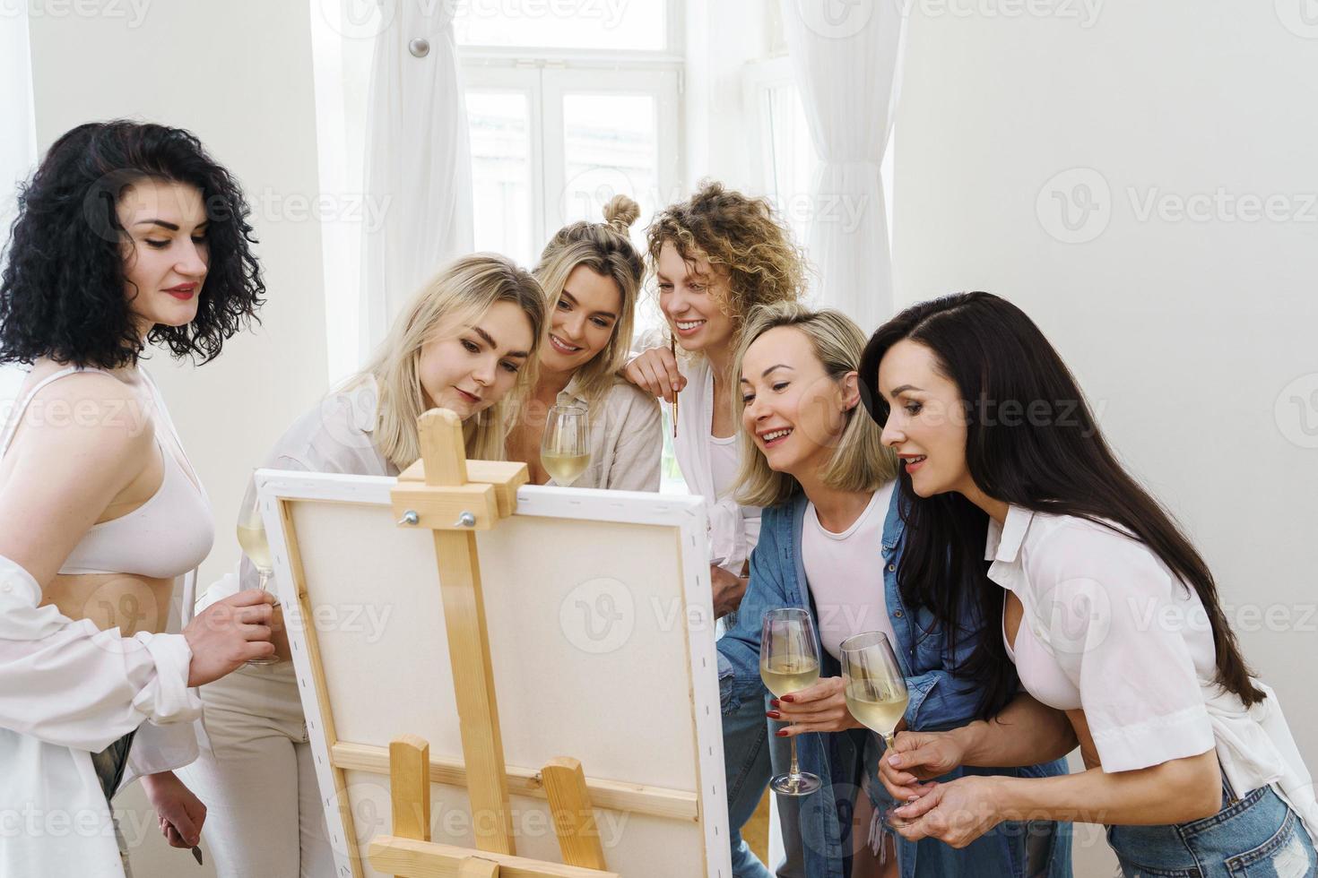 groupe de femmes peignant sur toile et buvant du vin blanc pendant la fête à la maison photo