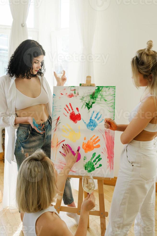 groupe de femmes peignant sur toile et buvant du vin blanc pendant la fête à la maison photo