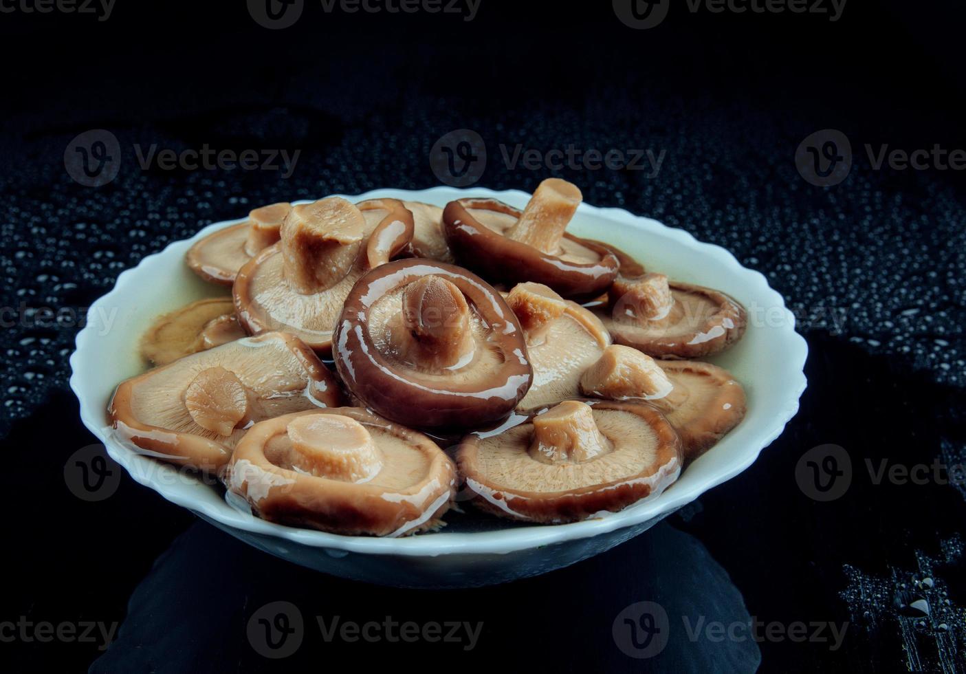 champignons salés dans une assiette sur fond noir. champignon de lait noir mariné . photo