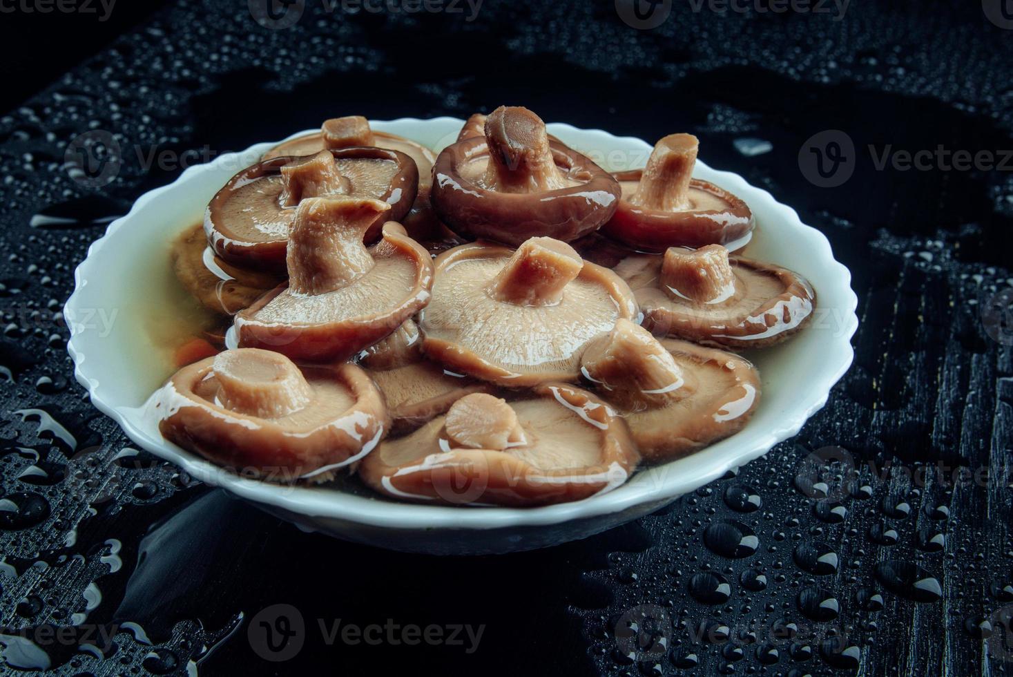 champignons salés dans une assiette sur fond noir. champignon de lait noir mariné . photo