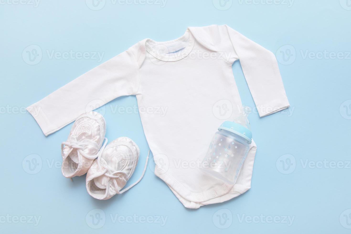 body pour nouveau-né, biberon et chaussons sur fond bleu photo