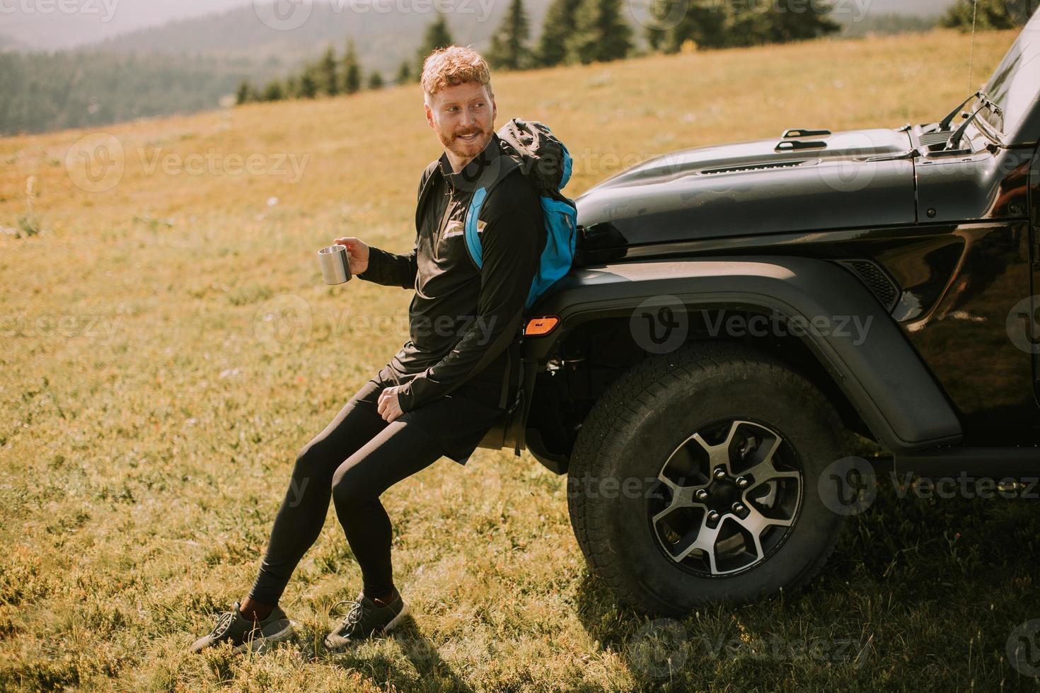 jeune homme se détendre et boire du café par le capot du véhicule tout-terrain à la campagne photo