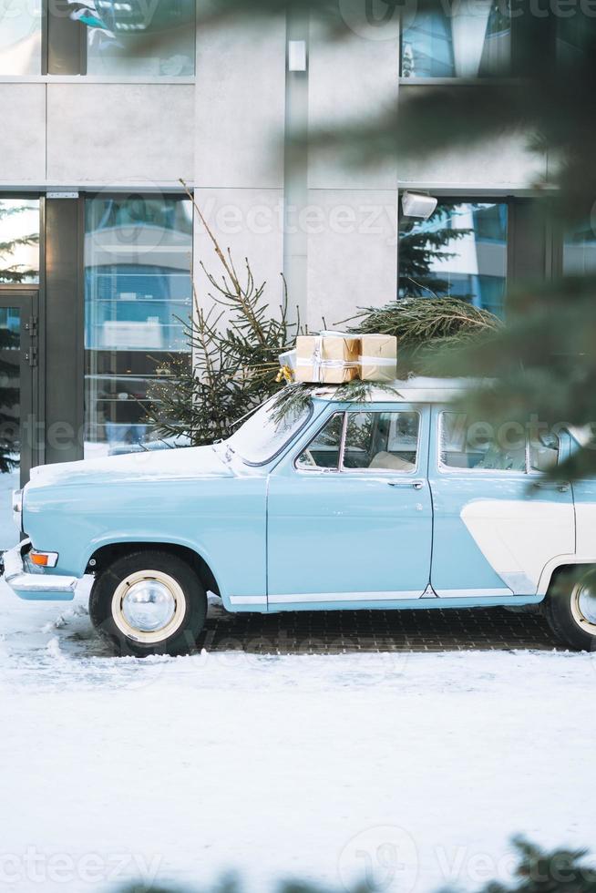 voiture bleu clair vintage décorée d'arbre de noël naturel et de boîtes avec des cadeaux dans la rue d'hiver photo