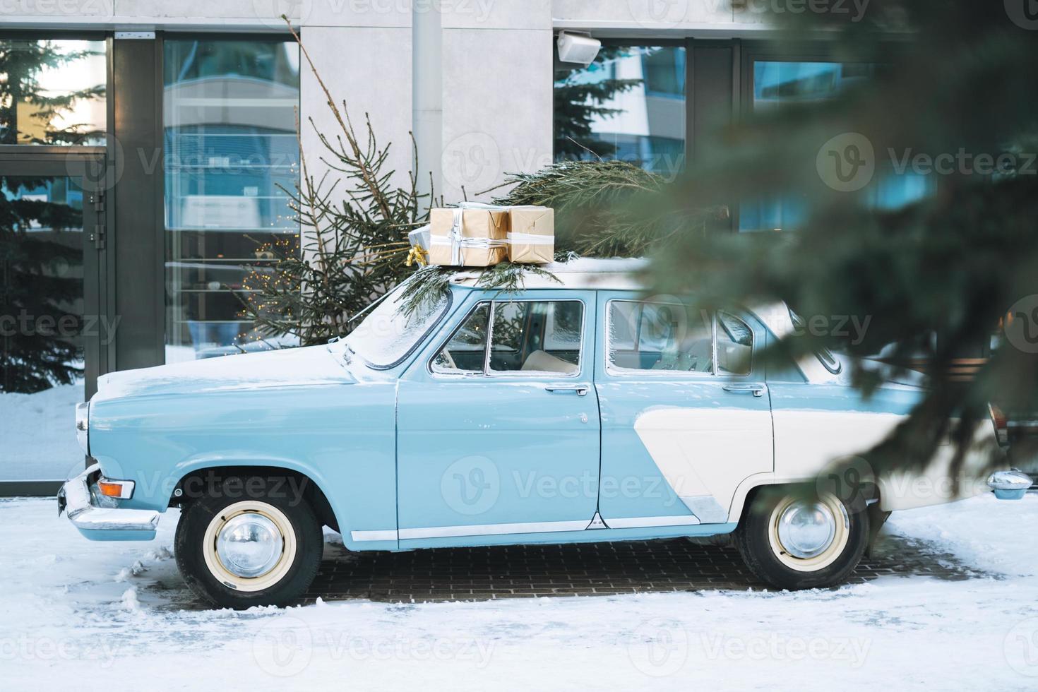 voiture bleu clair vintage décorée d'arbre de noël naturel et de boîtes avec des cadeaux dans la rue d'hiver photo