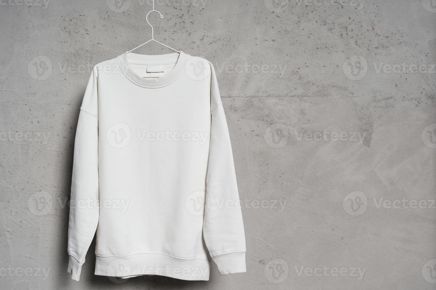 sweat-shirt blanc accroché au fin cintre métallique contre un mur de béton photo