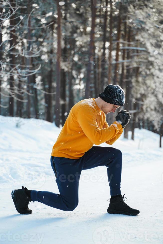 homme athlétique faisant des fentes pendant son entraînement d'hiver dans un parc enneigé photo