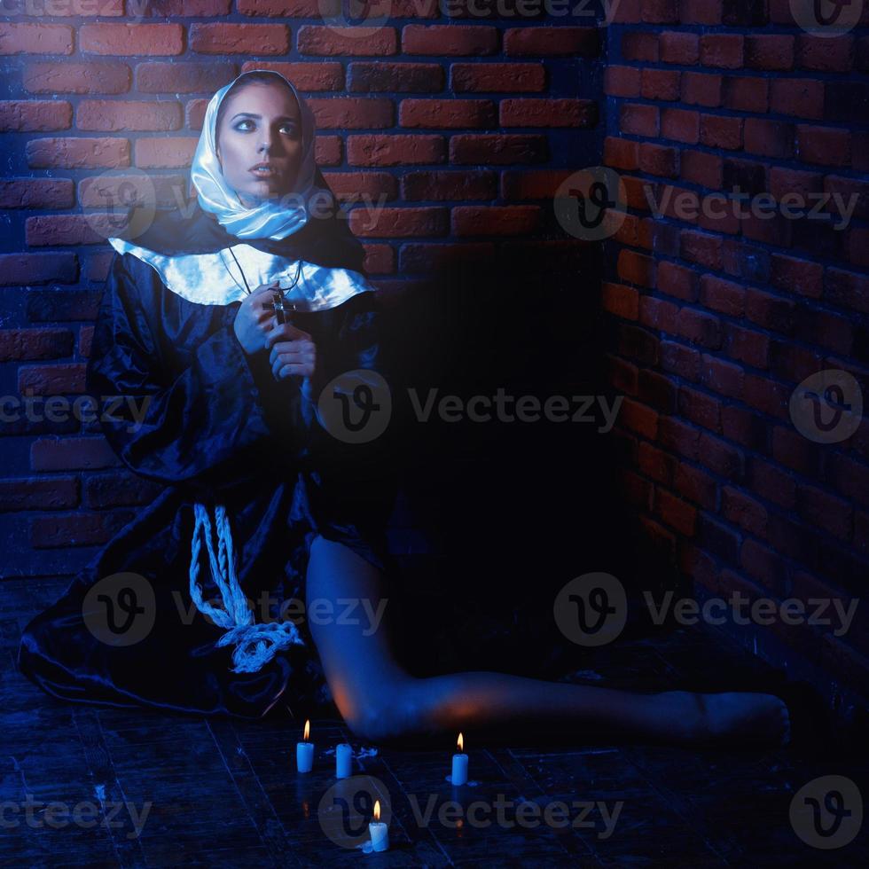 photo carrée d'une nonne près d'un mur de briques avec des bougies