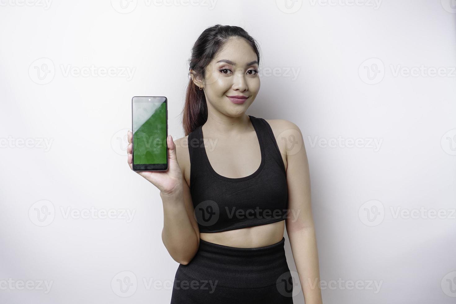 portrait d'une femme asiatique sportive portant un vêtement de sport et montrant un écran vert sur son téléphone, isolée sur fond blanc photo