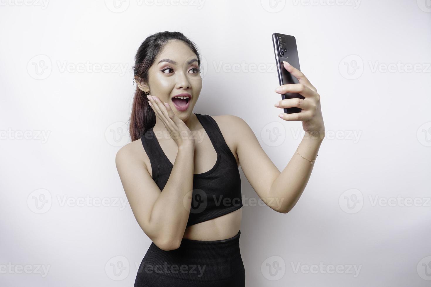 un portrait d'une femme asiatique sportive portant un vêtement de sport et tenant son téléphone, isolée sur fond blanc photo