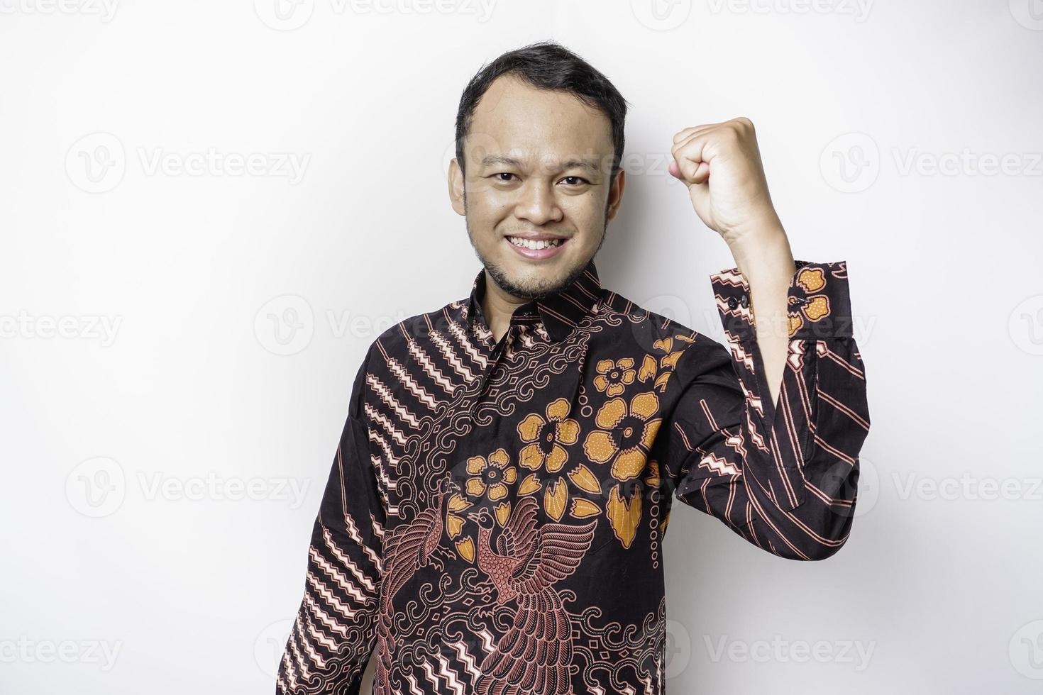 un jeune homme asiatique avec une expression heureuse et réussie portant une chemise batik isolée par fond blanc photo