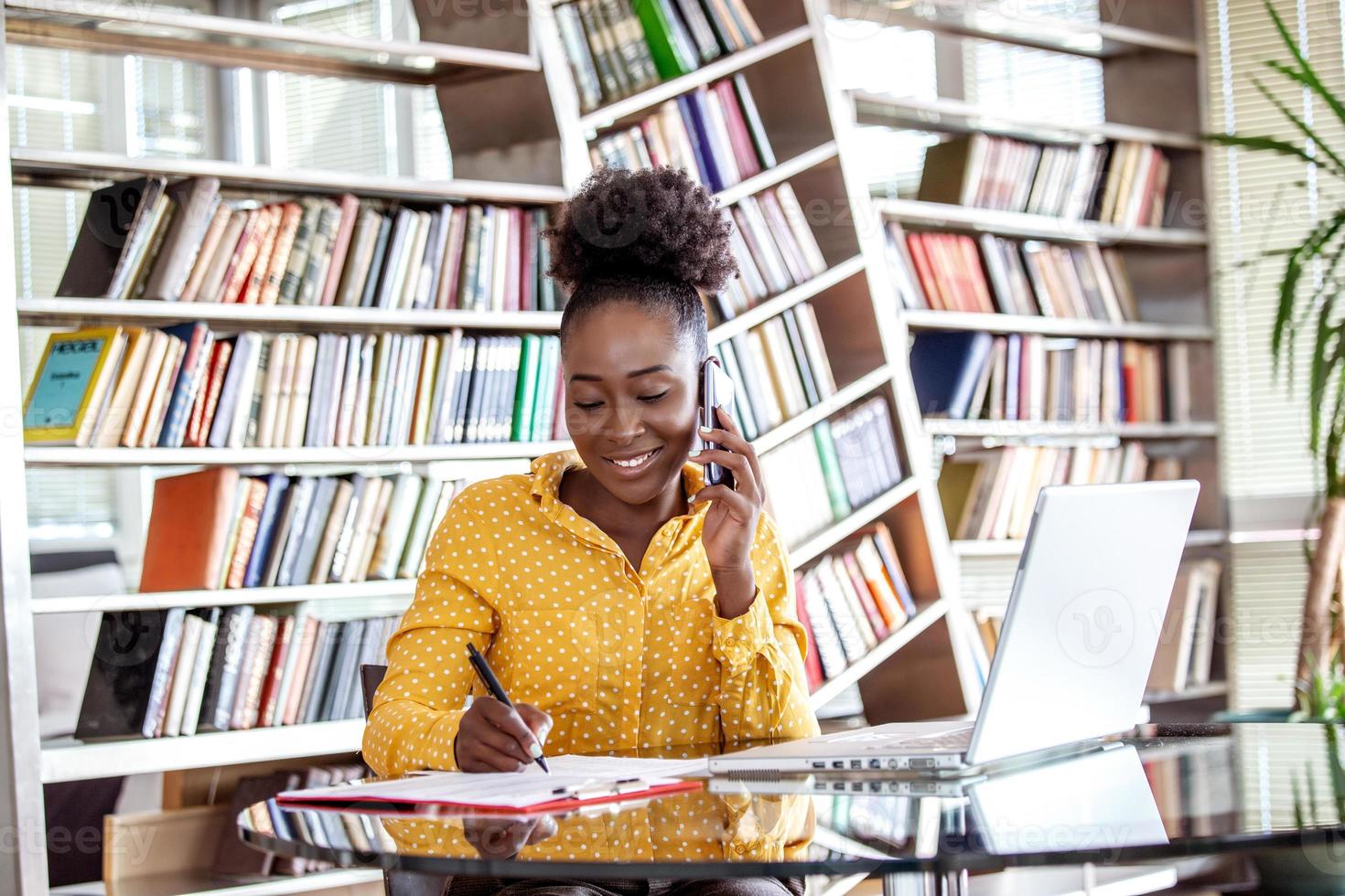 femme d'affaires prospère travaillant au bureau, femme afro-américaine parlant sur son téléphone portable et travaillant sur un ordinateur portable. concept d'entrepreneur de petite entreprise photo