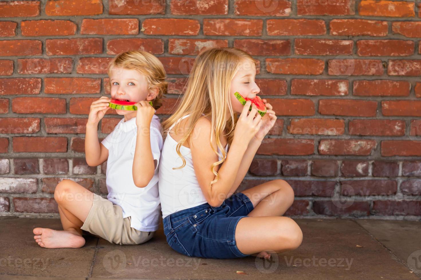 mignon jeune garçon et fille cuacasiens mangeant de la pastèque contre un mur de briques photo