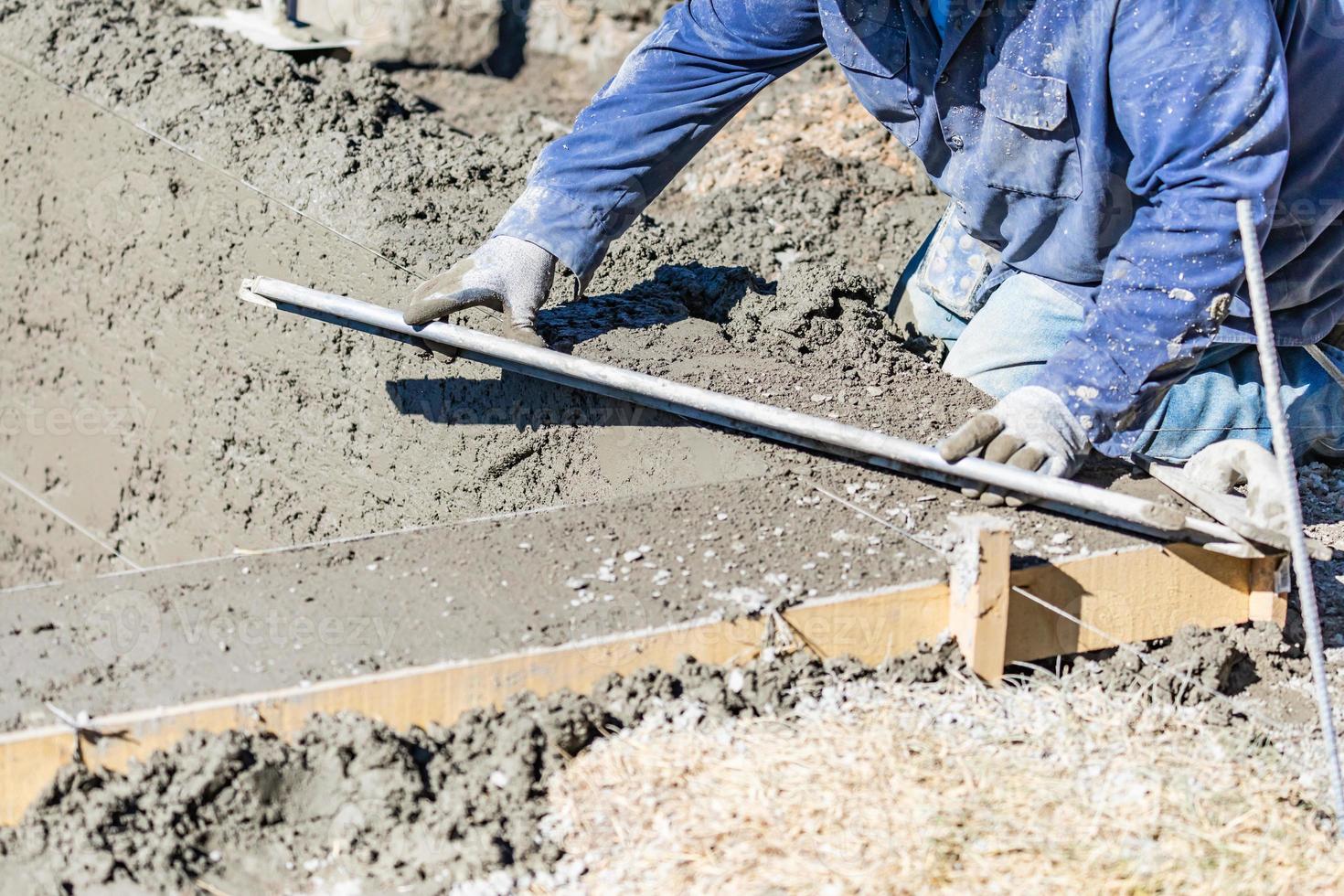 Ouvrier en construction de piscine travaillant avec une tige plus lisse sur du béton humide photo