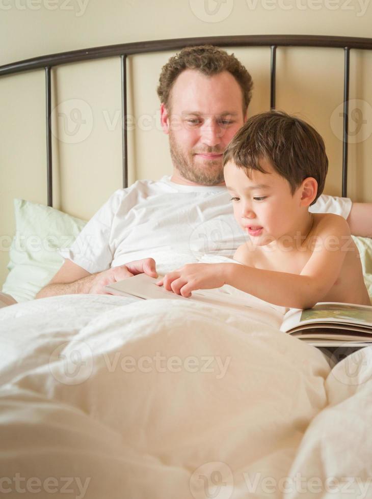 petit garçon chinois et caucasien lisant un livre au lit avec son papa photo