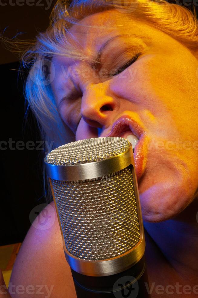 la chanteuse sous un éclairage gélifié chante avec passion dans un microphone à condensateur. photo