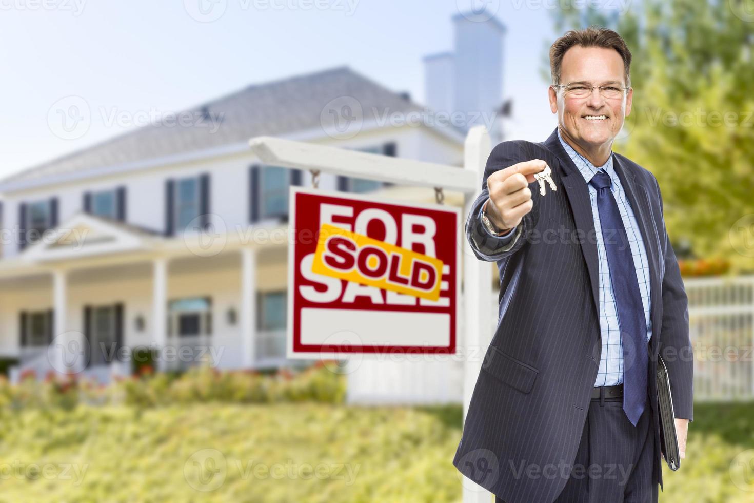 agent avec clés devant l'enseigne et la maison vendues photo