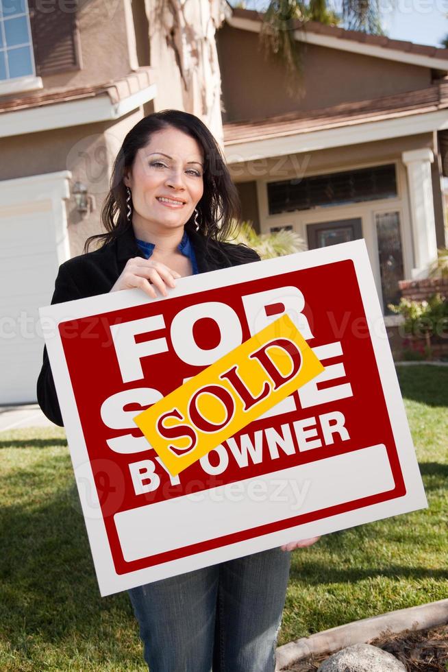 hispanic woman holding vendu à vendre par le propriétaire signe immobilier devant la maison photo