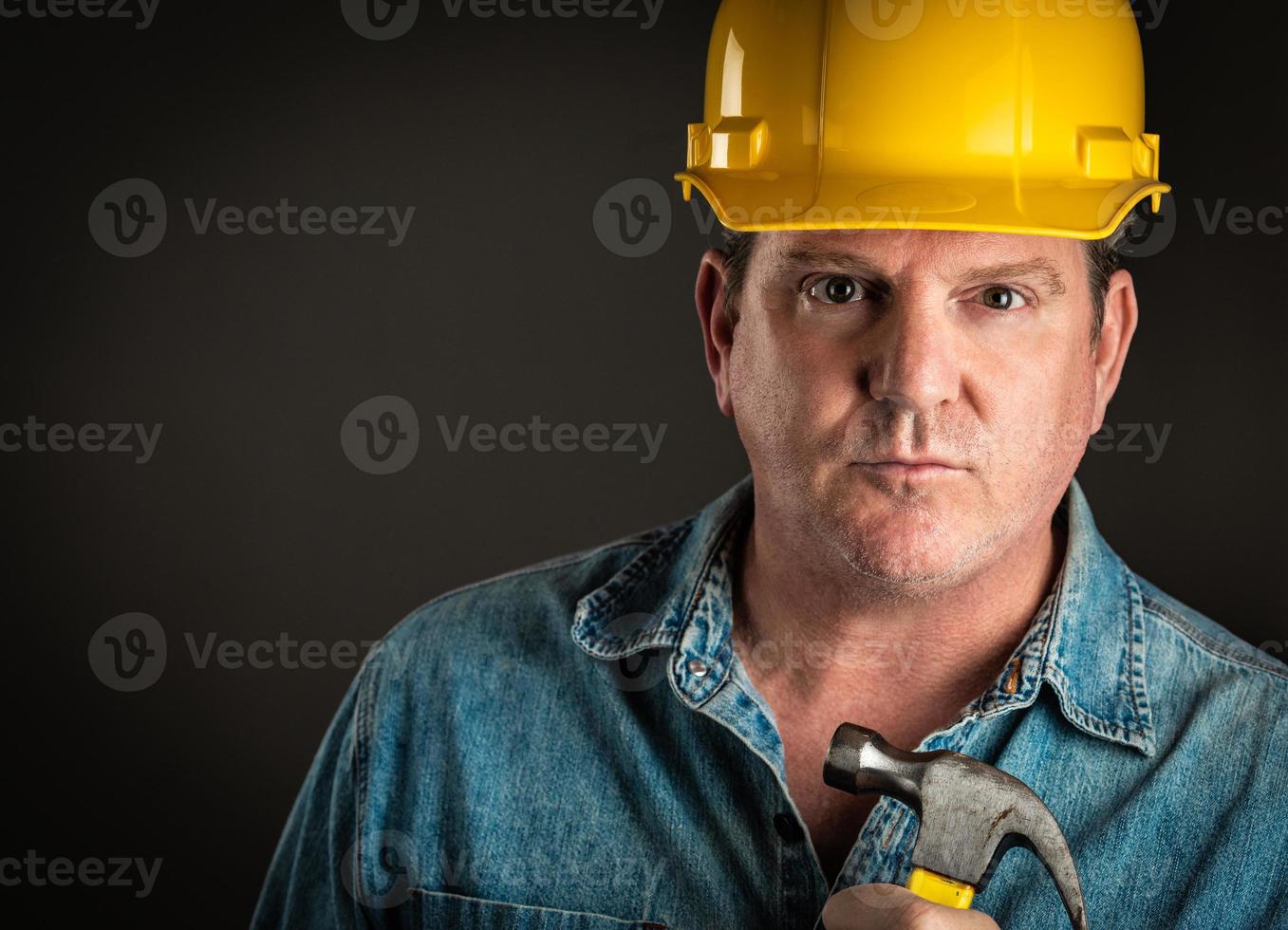 entrepreneur sérieux dans un casque tenant un marteau avec un éclairage dramatique. photo