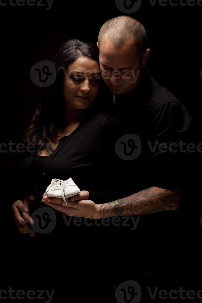 couple de race mixte tenant de nouvelles chaussures de bébé blanches sur fond noir photo