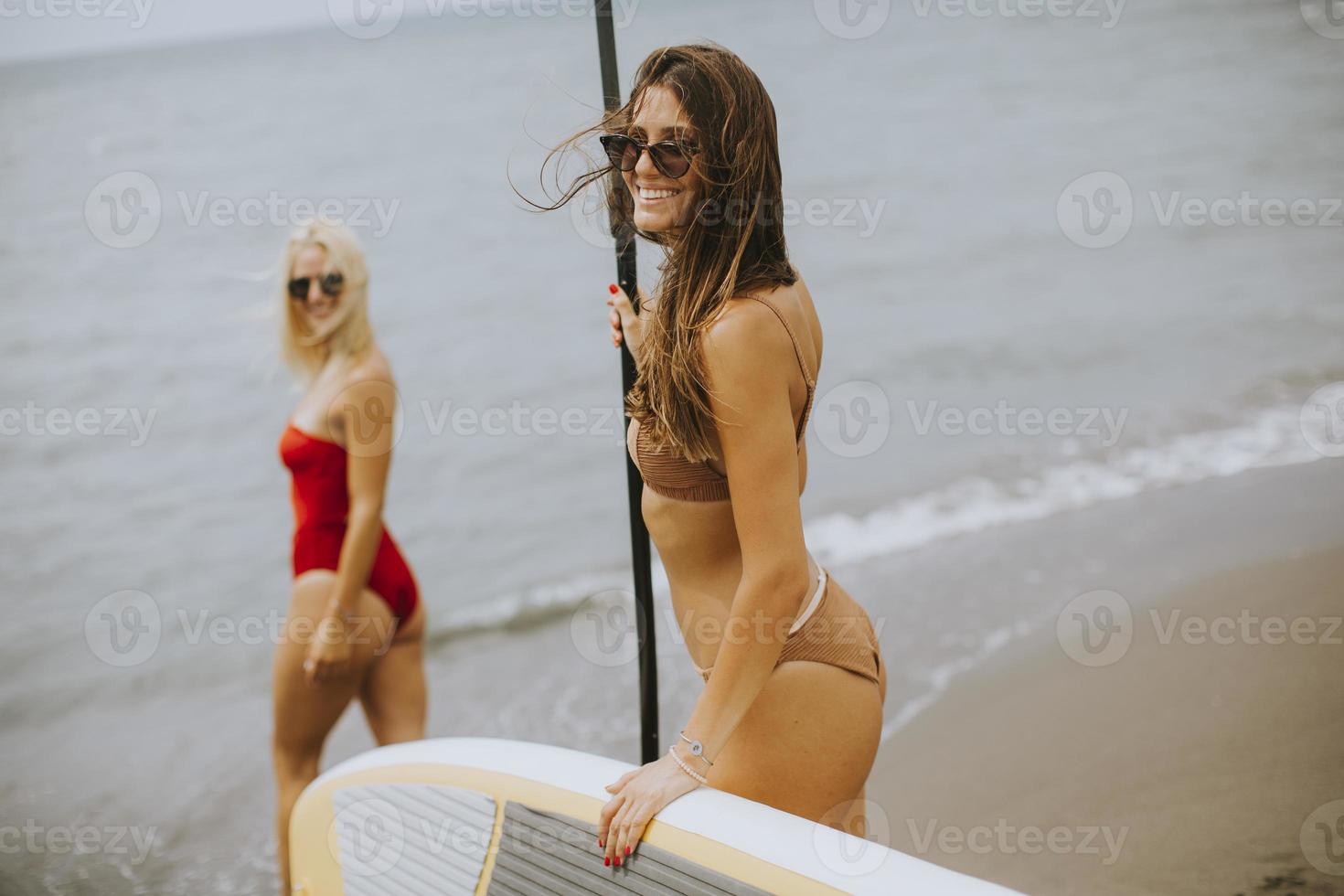 deux jeunes femmes avec paddle board sur la plage un jour d'été photo