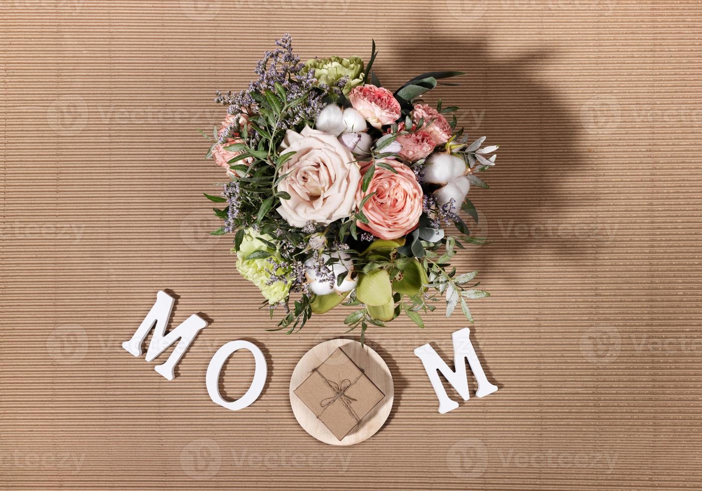 composition festive pour la fête des mères avec bouquet de fleurs, lettres blanches maman, coffret cadeau bricolage sur fond de carton beige. photo