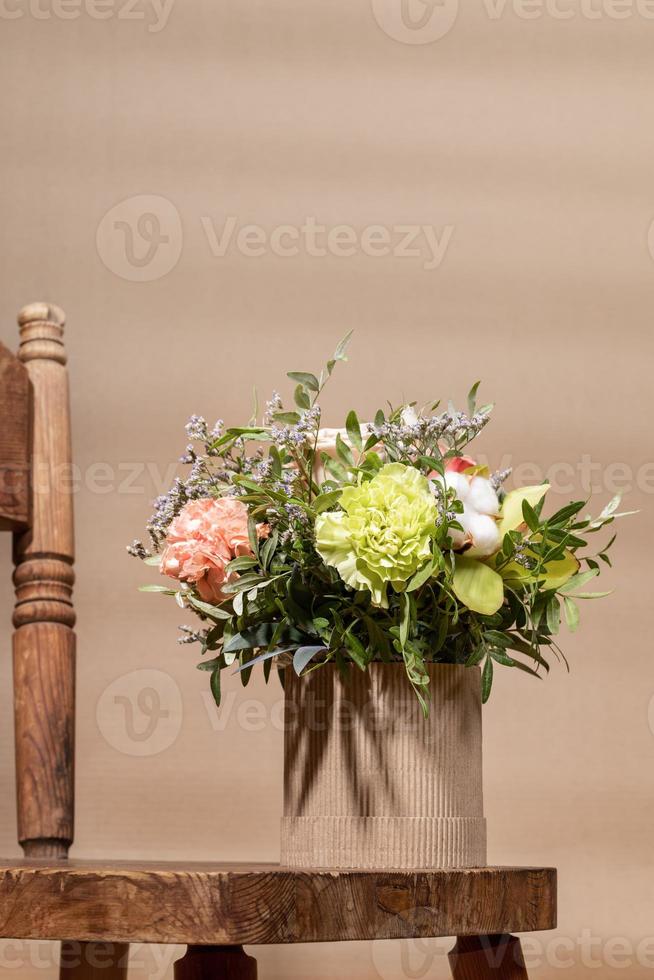 composition géométrique de vacances écologiques avec bouquet de fleurs dans un vase en carton bricolage et vieille chaise en bois sur beige. photo