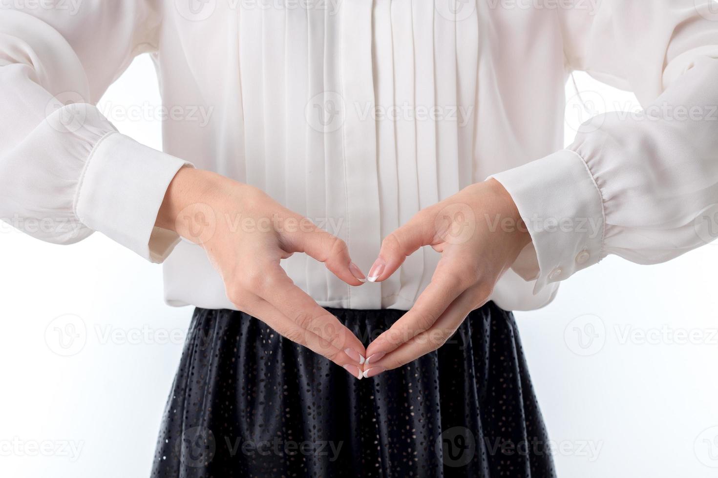 la fille dans le chemisier blanc se tenant la main devant et montre le coeur des doigts photo