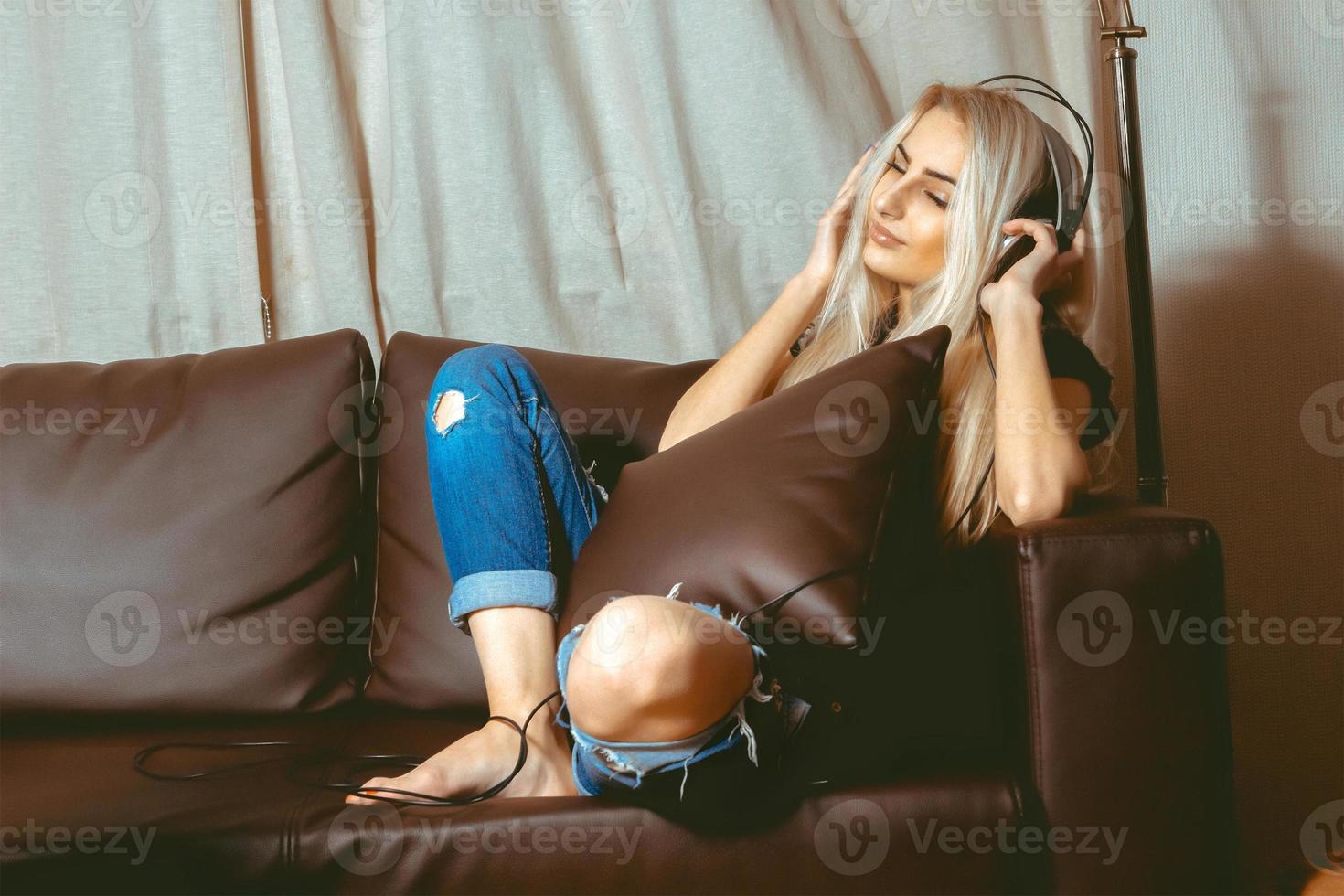 jeune fille blonde sensuelle écoutant de la musique dans les écouteurs et s'assoit sur le canapé photo