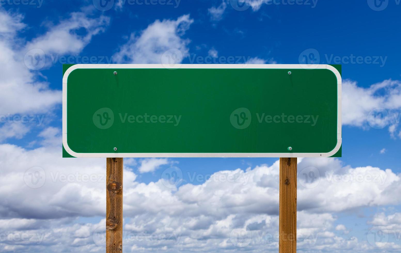 Panneau de signalisation vert vierge avec poteaux en bois sur ciel bleu et nuages photo