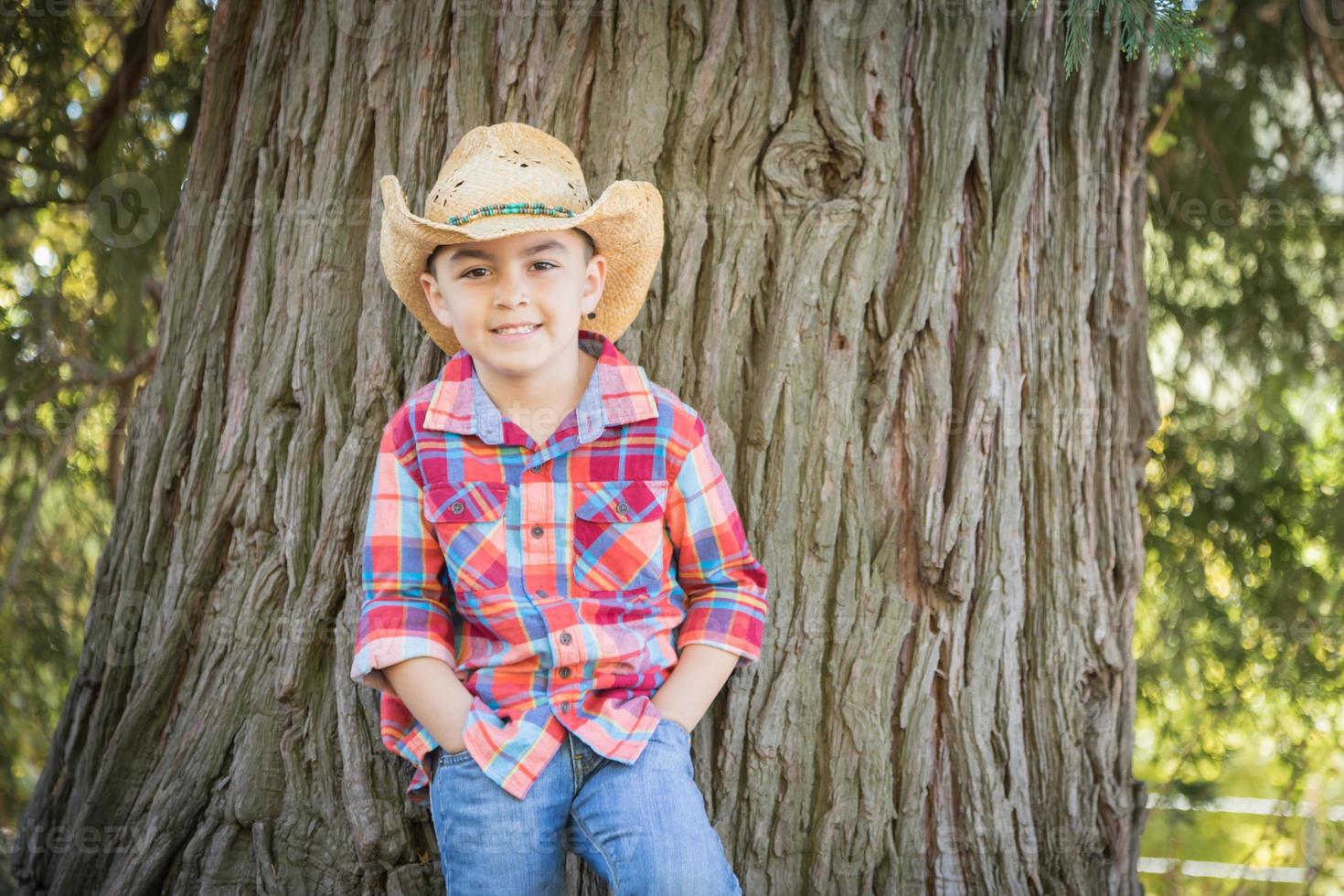 jeune garçon de race mixte portant un chapeau de cow-boy debout à l'extérieur. photo