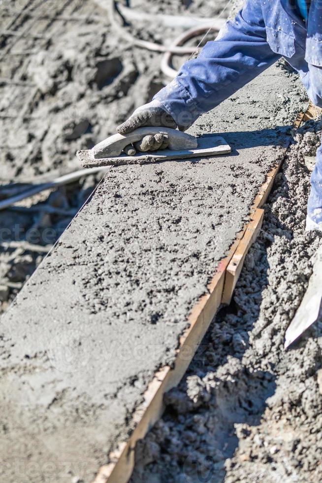 Ouvrier en construction de piscine travaillant avec un flotteur en bois sur du béton humide photo