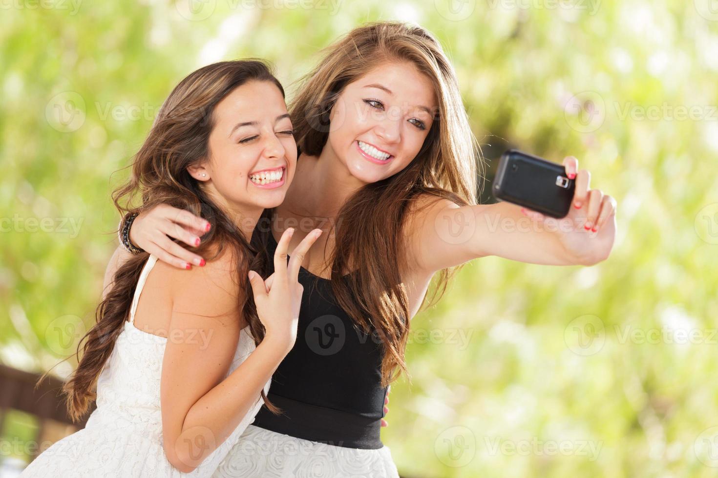 deux jolies copines métisses utilisant leurs téléphones portables intelligents pour un selfie à l'extérieur photo