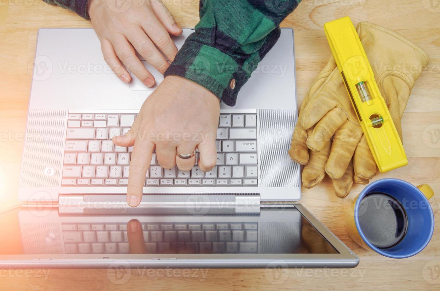 gants de travail, niveau à côté de l'entrepreneur pointant et examinant le projet sur un ordinateur portable photo